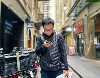 Portrait of young asian man using smart phone in laneway against buildings in the city.