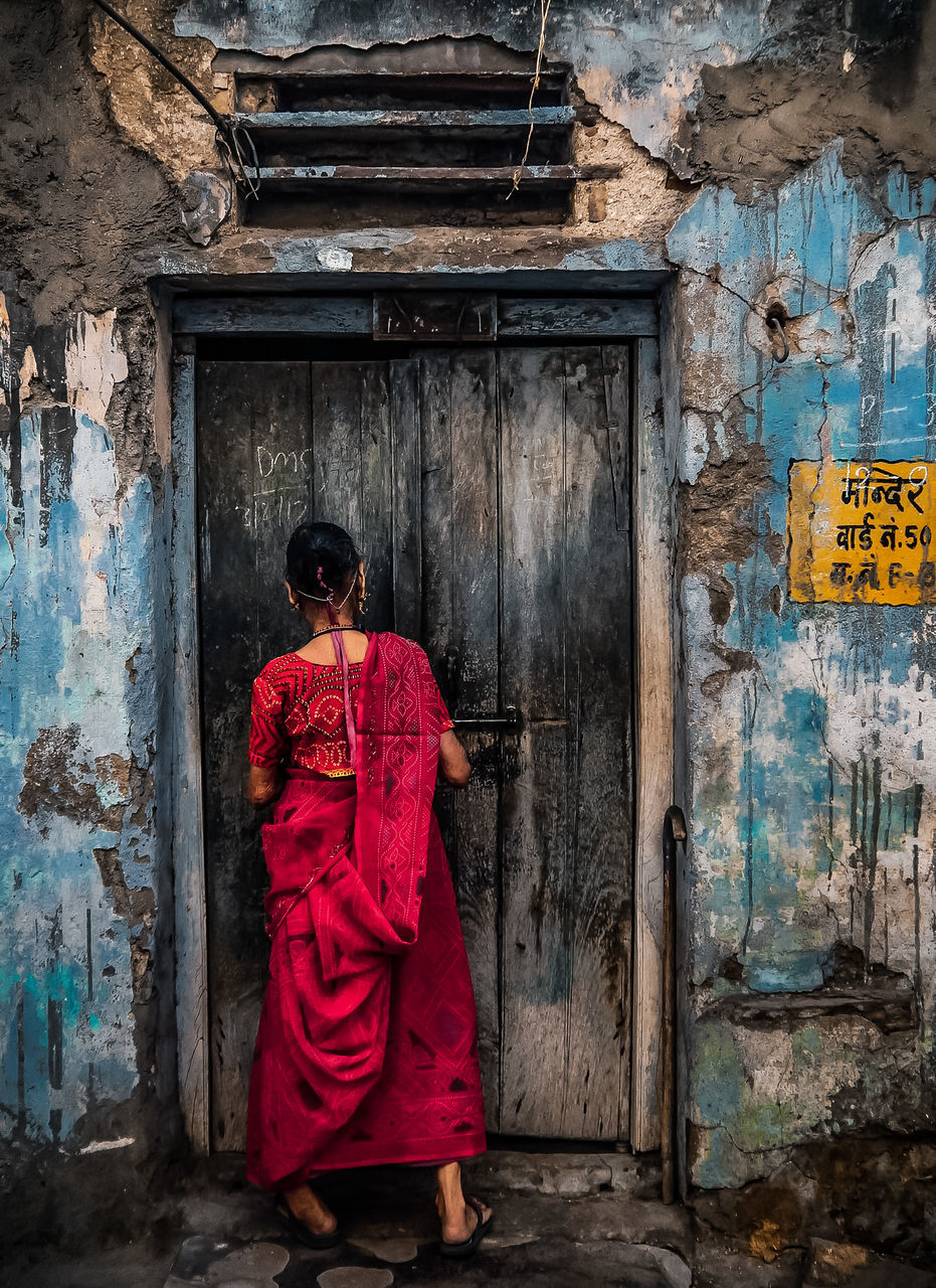 one person, full length, architecture, rear view, clothing, entrance, built structure, women, door, standing, real people, building, adult, day, weathered, building exterior, abandoned, old, traditional clothing, outdoors