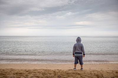 Rear view of boy standing at beach against sky