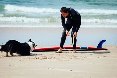 Full length of young man playing with dog on shore at beach