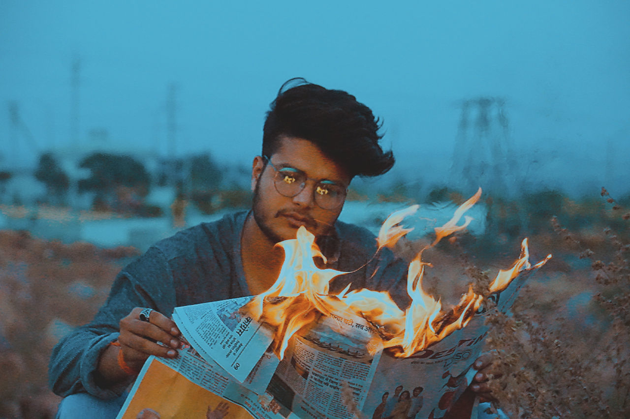 young adult, one person, real people, leisure activity, front view, young men, lifestyles, glasses, eyeglasses, activity, portrait, nature, burning, casual clothing, flame, focus on foreground, fire - natural phenomenon, outdoors, contemplation