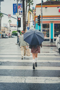 Fashionable young woman walks down a rainy street with a plain black umbrella, skirt and boots.