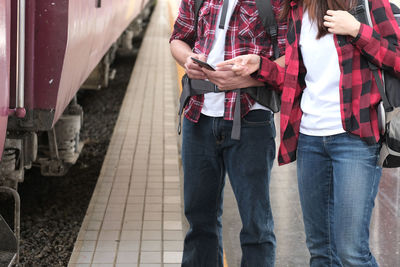 Midsection of couple using mobile phone at railroad station platform