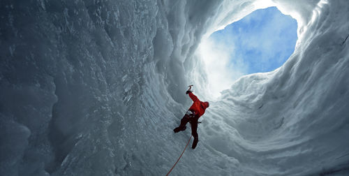 Man climbing towards an opening in an icecave at langjokull glacier