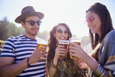 Man and women holding drink in glasses against sky