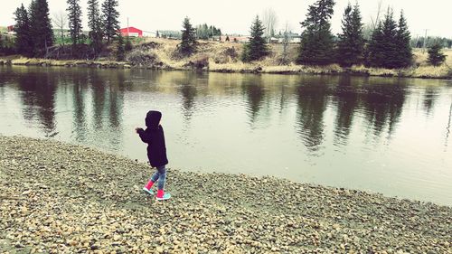 Rear view of girl standing by lake against sky