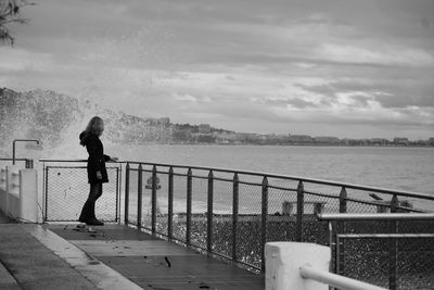 Woman standing on railing by sea against sky