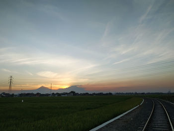 Railroad tracks on field against sky during sunset