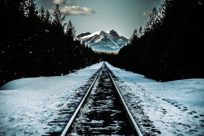 Snow covered railroad track by mountain against sky