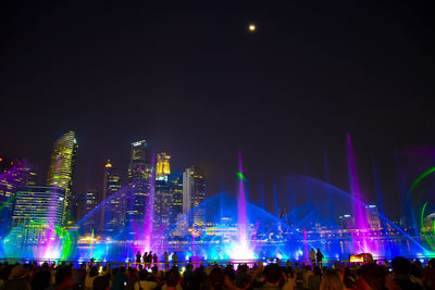Crowd at illuminated city against sky at night