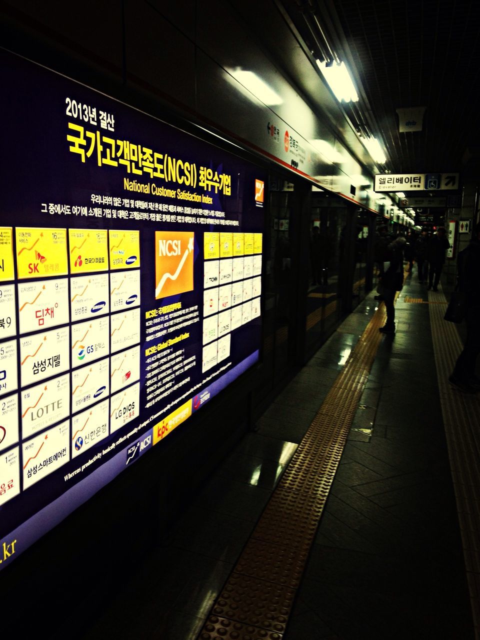 indoors, railroad station, public transportation, text, railroad station platform, illuminated, transportation, subway station, communication, rail transportation, western script, men, travel, railroad track, subway, information sign, architecture, subway platform, built structure