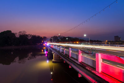 Light trails on bridge over city against sky at night