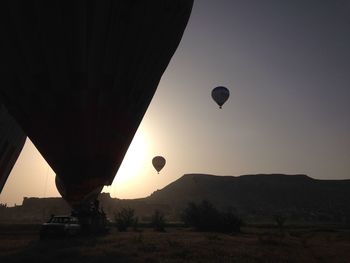 Hot air balloons flying over silhouette landscape against sky