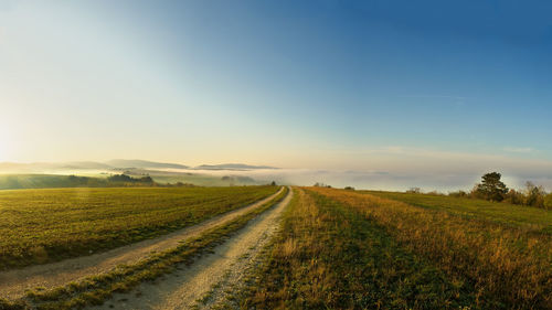 Dirt road amidst field against sky