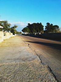 Road by trees against clear blue sky