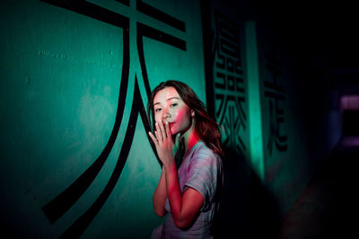 Young woman standing against wall at night