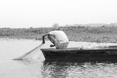 Rear view of man on boat in lake against sky