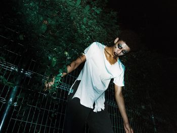 Portrait of young man standing by railing at night