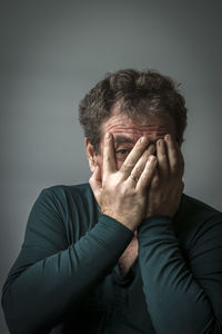 Portrait of man covering face against gray background