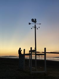 Silhouette street light on beach against clear sky during sunset