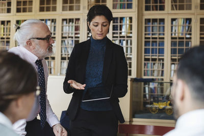 Woman holding digital tablet while standing in meeting at library