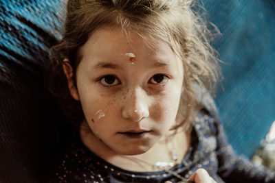 Close-up portrait of serious girl with paints on her face at home