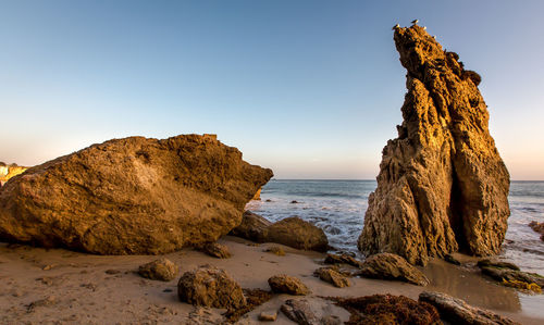 Rock formation on beach against clear sky