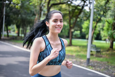 Portrait of young woman running on road against trees