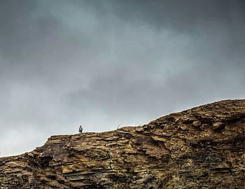 Low angle view of man standing on cliff against sky