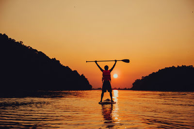 Silhouette person standing in sea against sky during sunset