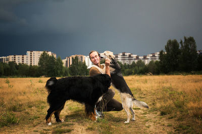 Man playing with dogs on land against sky