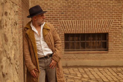 Portrait of adult man in hat and coat against wall on street