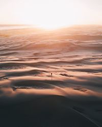 Mid distance of man walking on sand against sky during sunset