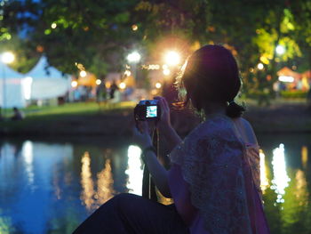 Woman photographing by lake at night