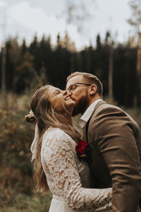 Side view of young couple standing against trees