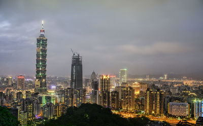 Illuminated buildings in city against cloudy sky