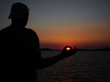 Rear view of silhouette man in sea against sky during sunset