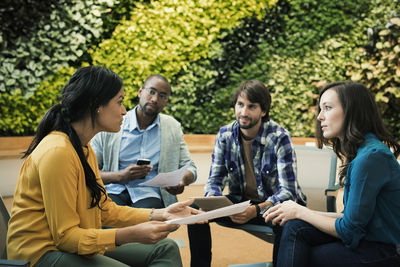 Young business people discussing in front of green plant wall