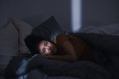 Pensive young woman lying in bed