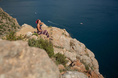 High angle view of man sitting on rock by sea