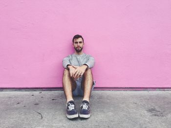 Portrait of young man sitting against wall