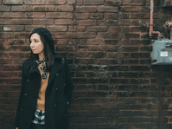 Portrait of young woman standing against brick wall