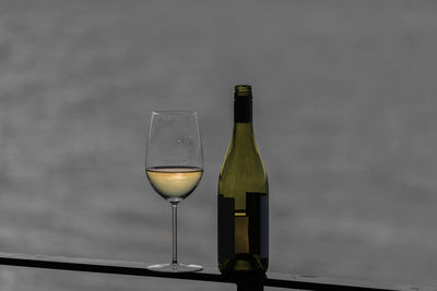 Close-up of bottle and wineglass on railing against sea