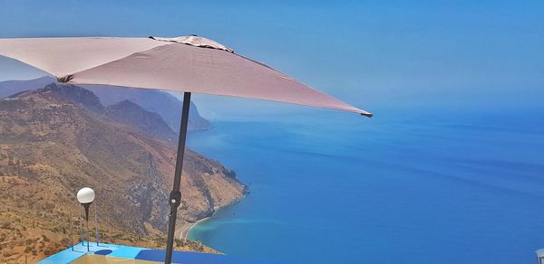 Beach umbrella by sea against clear blue sky