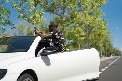 Young african man taking a picture with his smartphone next to his car