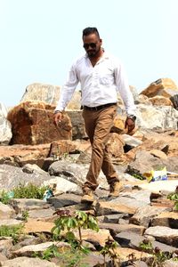 Young man standing on rock against sky