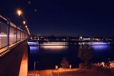 Illuminated bridge over river against sky at night