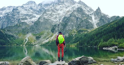 Rear view of man standing by lake against mountain