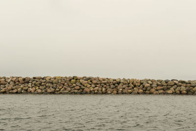 Stone wall by sea against clear sky