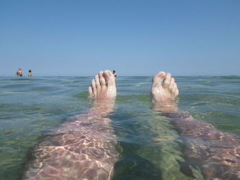 Low section of person swimming in sea against clear sky